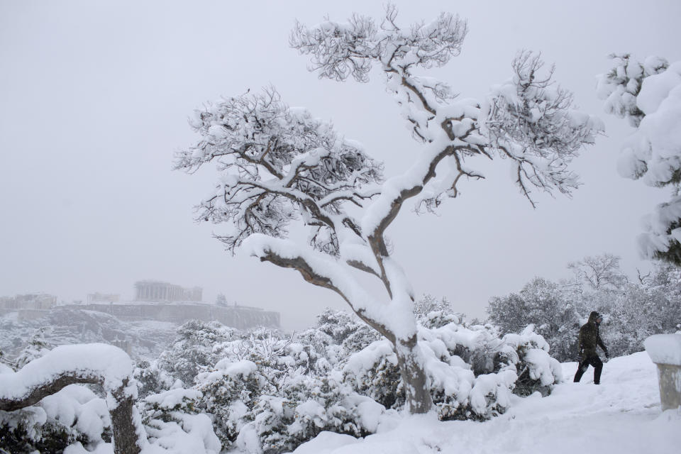 A man walks at Filopapos hill as snow falls, with the ancient Acropolis hill and the Parthenon temple, in background, Athens, on Tuesday, Feb. 16, 2021. There have been record subzero temperatures in Texas and Oklahoma, and Greenland is warmer than normal. Snow fell in Greece and Turkey. Meteorologists blame the all-too-familiar polar vortex. (AP Photo/Petros Giannakouris)