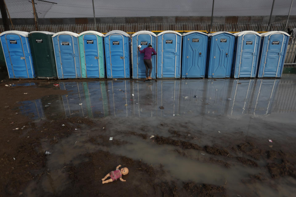 A woman searches a shower and rain flooded area for a toilet in acceptable condition at a sports complex sheltering thousands of Central Americans hoping to enter the U.S., in Tijuana, Mexico, Thursday, Nov. 29, 2018. Aid workers and humanitarian organizations expressed concerns Thursday about the unsanitary conditions at the sports complex in Tijuana where more than 6,000 Central American migrants are packed into a space adequate for half that many people and where lice infestations and respiratory infections are rampant. (AP Photo/Rebecca Blackwell)