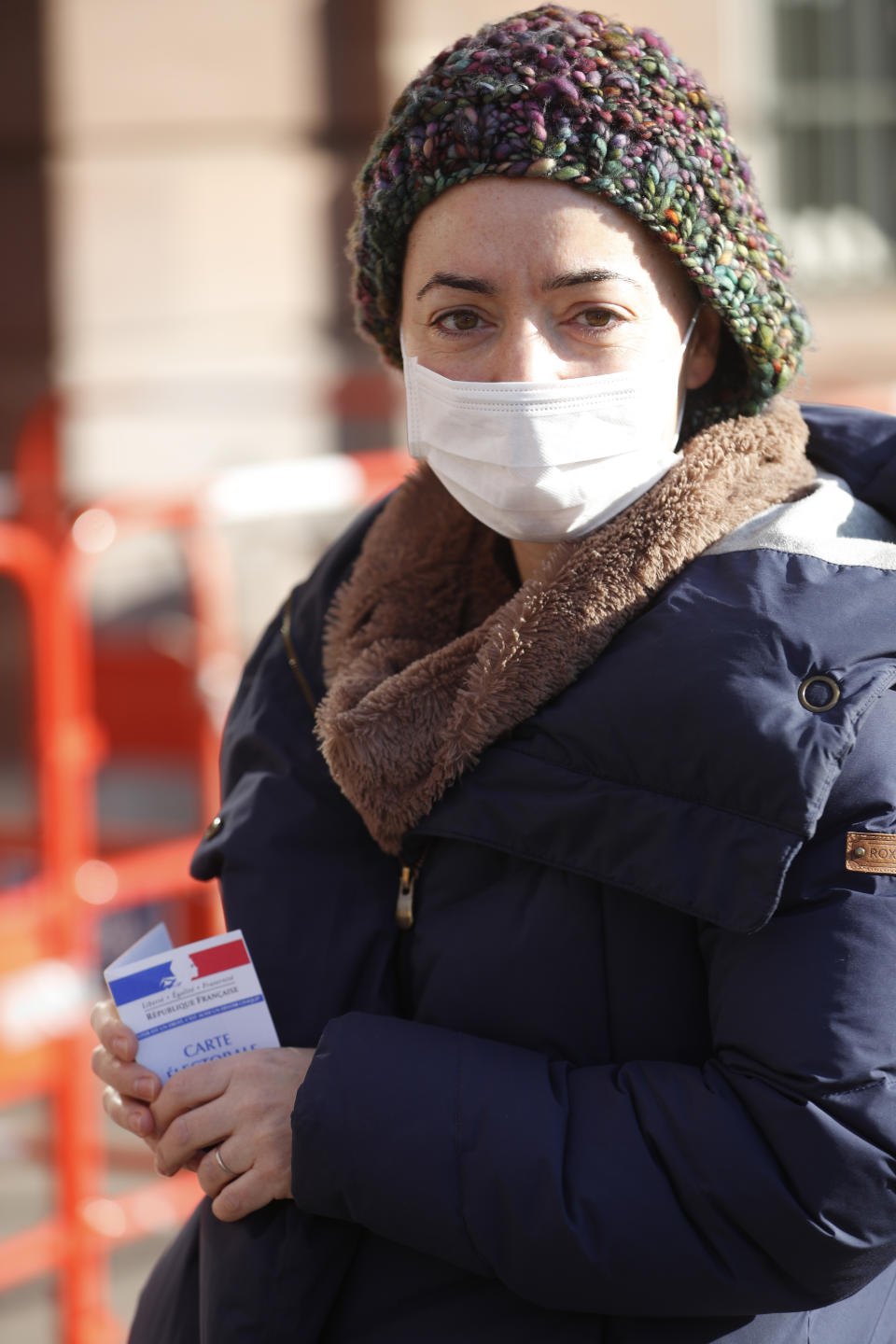 A woman wearing a face mask holds her voting card before voting in the first round of the municipal elections, in Strasbourg, eastern France, Sunday March 15, 2020. The new virus has shuttered all schools, banished cheek-kissing and upended daily life across France, but President Emmanuel Macron won't let it disrupt democracy, so he's maintaining nationwide elections this weekend. For most people, the new coronavirus causes only mild or moderate symptoms. For some it can cause more severe illness. (AP Photo/Jean-Francois Badias)
