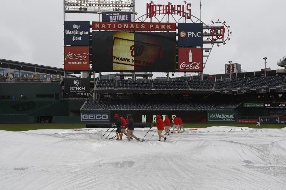 A grounds crew removes water from a tarp before a baseball game between the Philadelphia Phillies and Washington Nationals, Sunday, Oct. 2, 2022, in Washington. (AP Photo/Luis M. Alvarez)