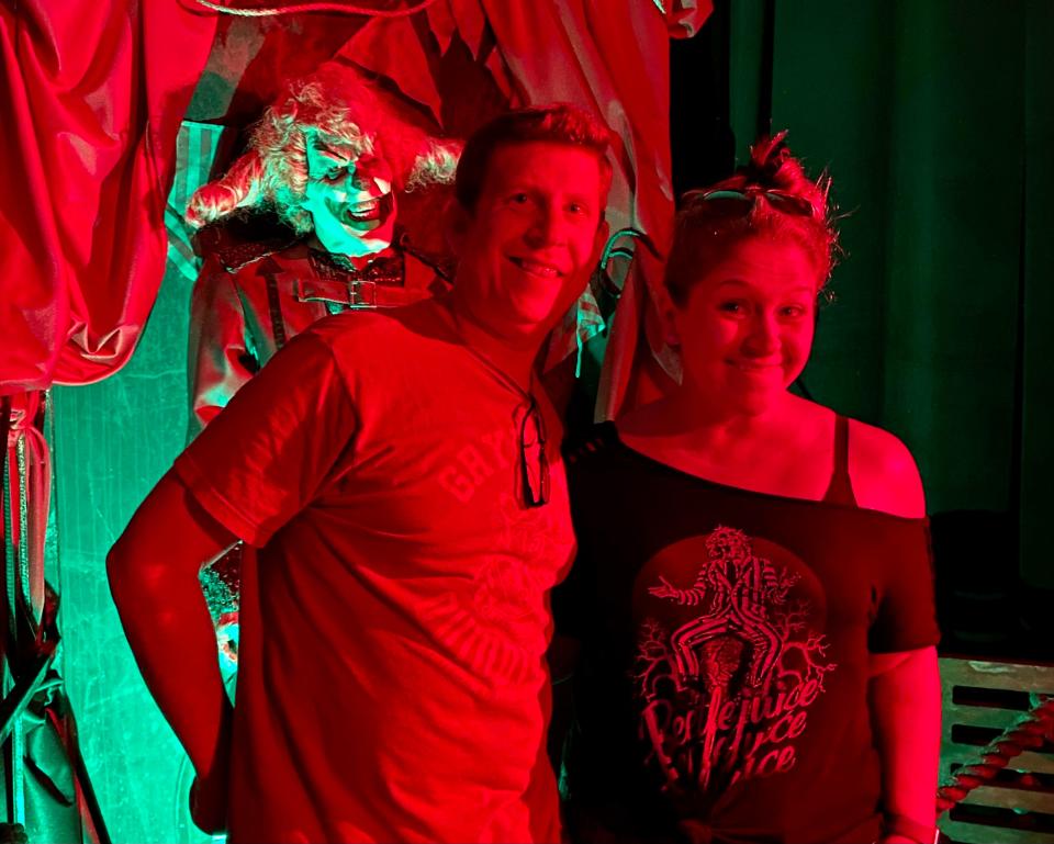 The author (right) and her husband at Halloween Horror Nights, lit up by red lights, with a clown behind them