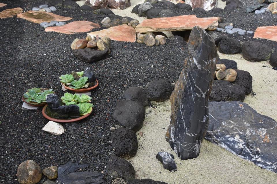 Zen garden containing lava rock, sand, and succulent plants in terracotta dishes