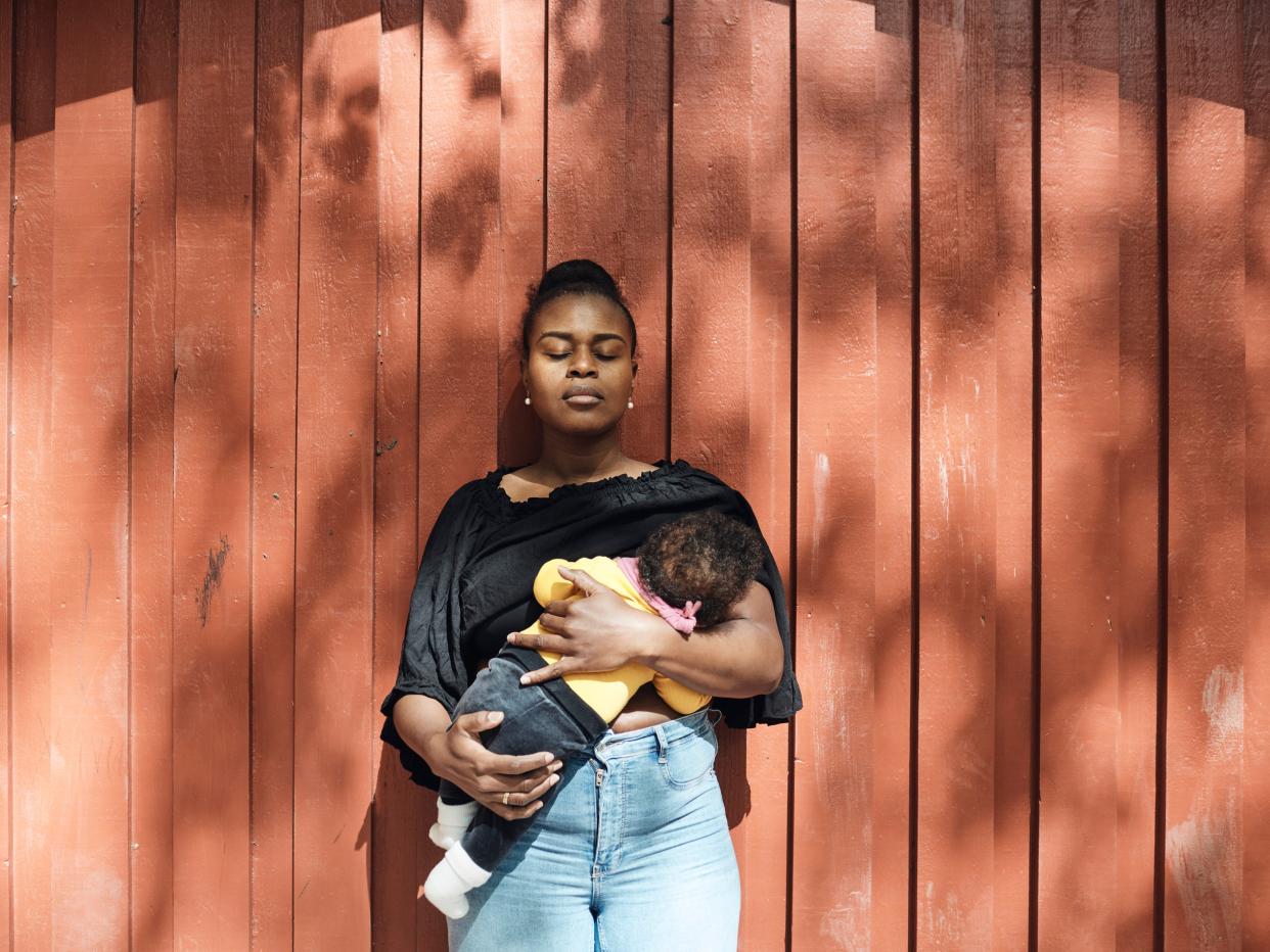 Woman holding her baby up to breast feed against a sunny backdrop.