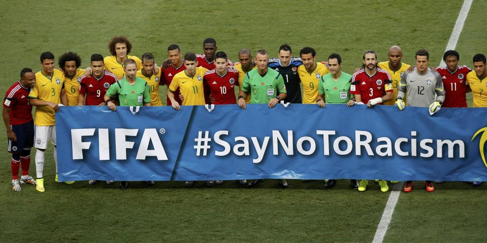 Brazil's (in yellow) and Colombia's national soccer players (in red) stand with officials behind a banner before kickoff during the 2014 World Cup quarter-finals at the Castelao arena in Fortaleza July 4, 2014. REUTERS/Leonhard Foeger