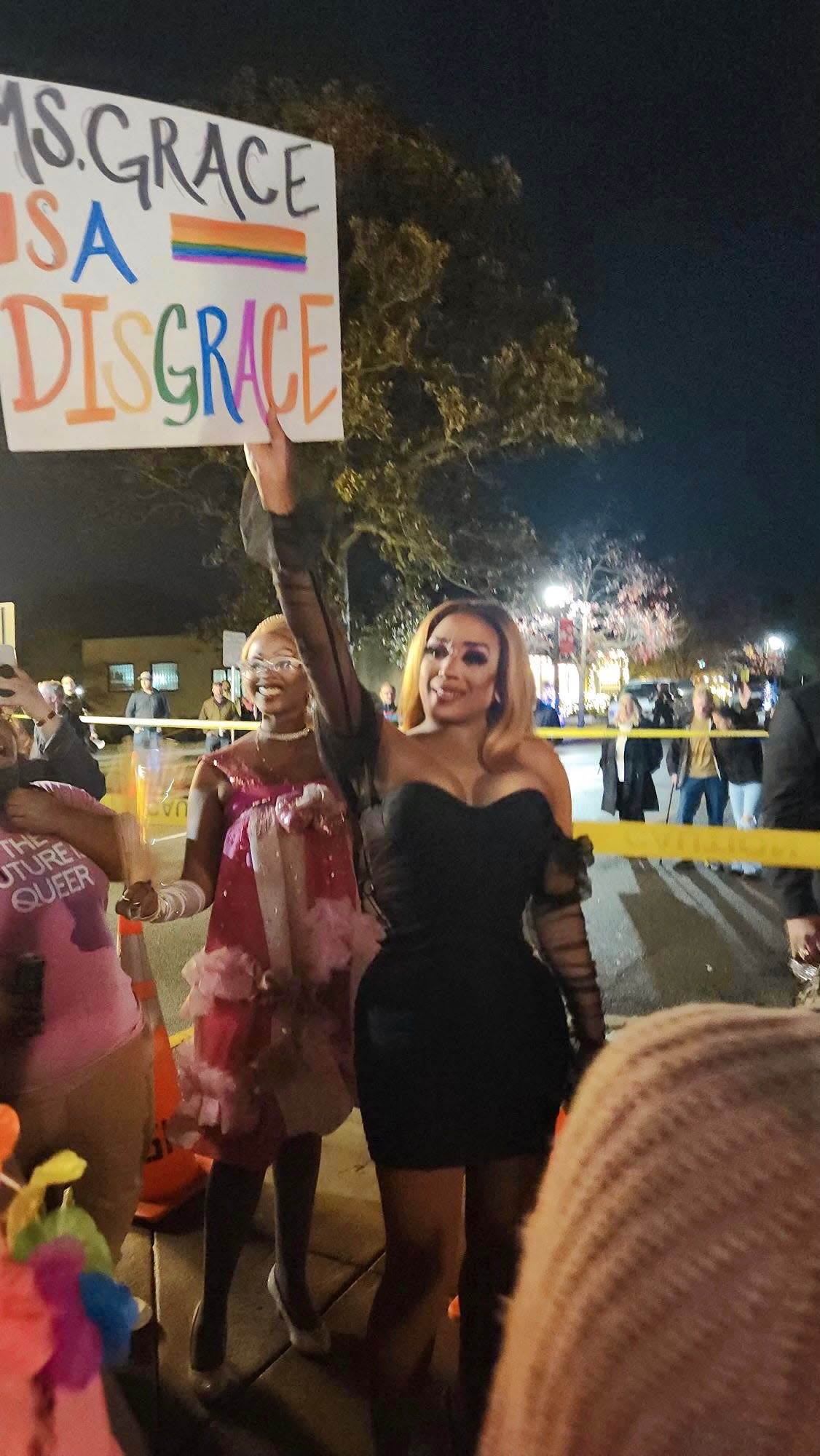 Drag artist Naomi Dix pose with a sign that reads "Ms. Grace is a disgrace" at Downtown Divas drag show at Sunrise Theater in Southern Pines, Dec. 3, 2022.