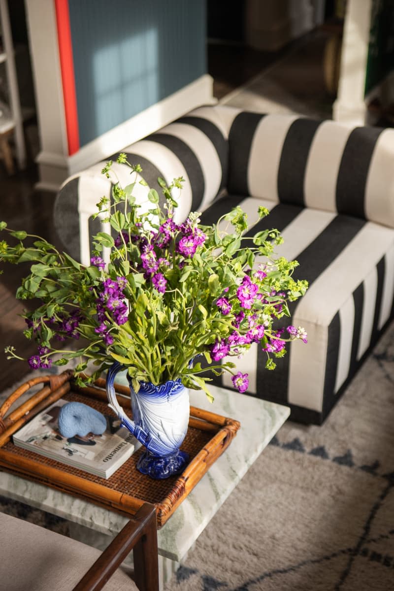 detail of vase of purple flowers on table in front of black and white striped chair