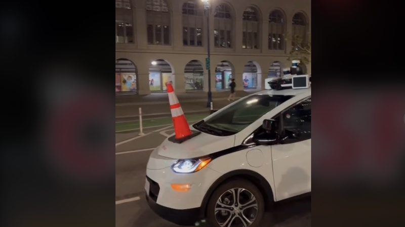 A Cruise self-driving vehicle disabled by a traffic cone on its hood.  