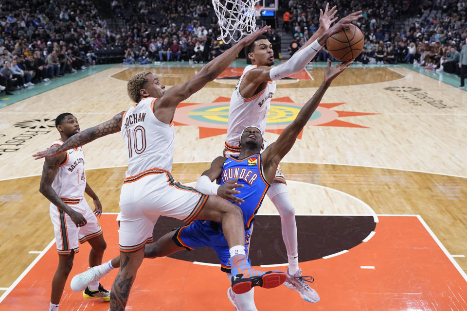 Oklahoma City Thunder guard Shai Gilgeous-Alexander (2) is blocked as he drives to the basket between San Antonio Spurs forward Jeremy Sochan (10) and center Victor Wembanyama (1) during the first half of an NBA basketball game in San Antonio, Wednesday, Jan. 24, 2024. (AP Photo/Eric Gay)