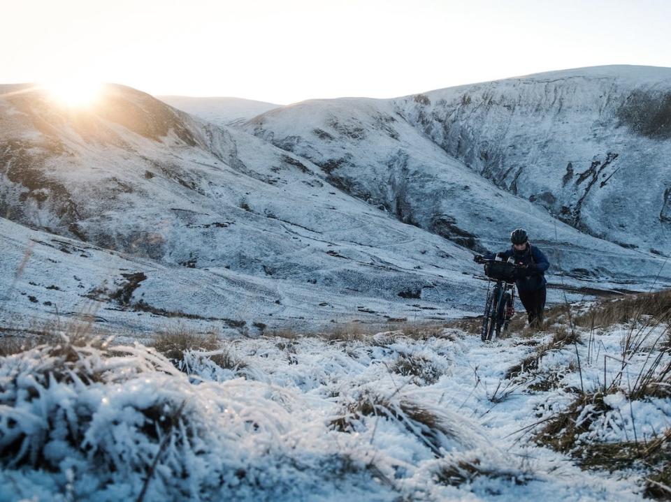 Sarah Morgan pushes her bicycle in a snowy field on a cycling trip.