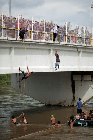 Honduran migrants, part of a caravan trying to reach the U.S., jump and climb down from the bridge that connects Mexico and Guatemala to avoid the border checkpoint as others look while queueing to enter Mexico, in Ciudad Hidalgo, Mexico October 19, 2018. REUTERS/Ueslei Marcelino