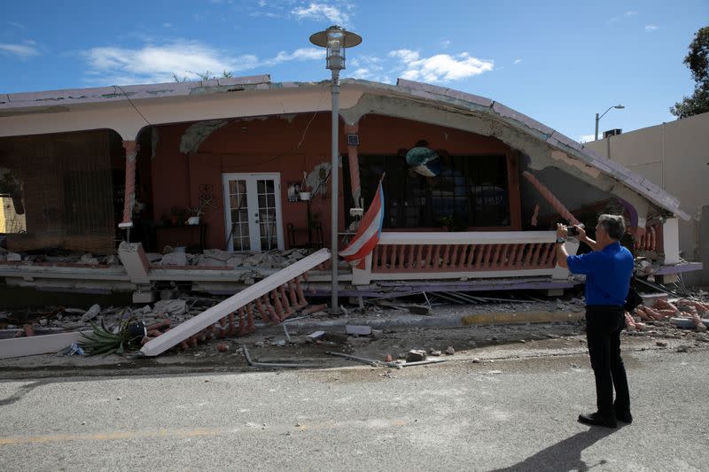 A man uses his phone to take photos of a house that collapsed on its foundation after an earthquake in Guanica