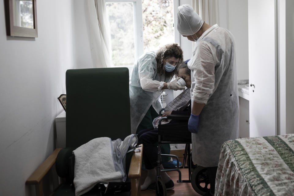 FILE - In this April 9, 2020, file photo, elderly residency workers Celia, left, and Patricia, right, feed Carmen at "Las Praderas" elderly care home in Pozuelo de Alarcon, outskirts of Madrid. Countries across Europe are struggling amid the coronavirus pandemic with the dilemma of leaving the elderly and others near death in enforced solitude or whether to allow some personal contact with relatives. At nursing homes, everything is done to keep out visitors who might be infected, and family members are almost always banned from coming to see their loved ones. (AP Photo/Bernat Armangue, File)