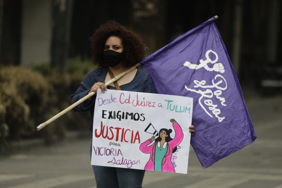 A woman holds a feminist flag and a sign that reads in Spanish "From Ciudad Juarez to Tulum we demand justice for Victoria Salazar," during a protest outside of the Quintana Roo state offices in Mexico City, Monday, March. 29, 2021. The demonstrators were protesting the police killing in Tulum, Quintana Roo state, of Salvadoran national Victoria Esperanza Salazar when a female police officer knelt on her back to cuff her. Mexican authorities say an autopsy confirmed that police broke her neck. (AP Photo/Eduardo Verdugo)