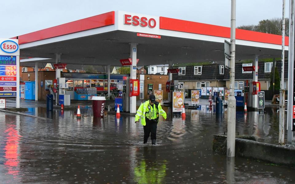A police officer wades through flood water at the forecourt of an Esso garage in Bridport, Dorset