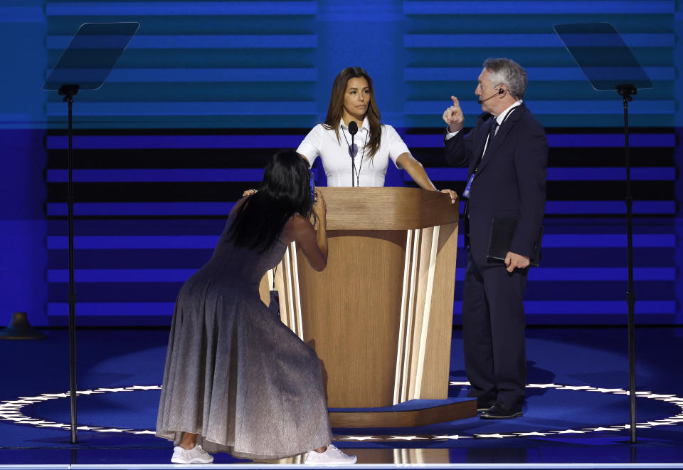 Mindy Kaling steht hinter einem Podium und spricht, Regina King kniet und macht ein Foto, und ein Mann im Anzug gestikuliert