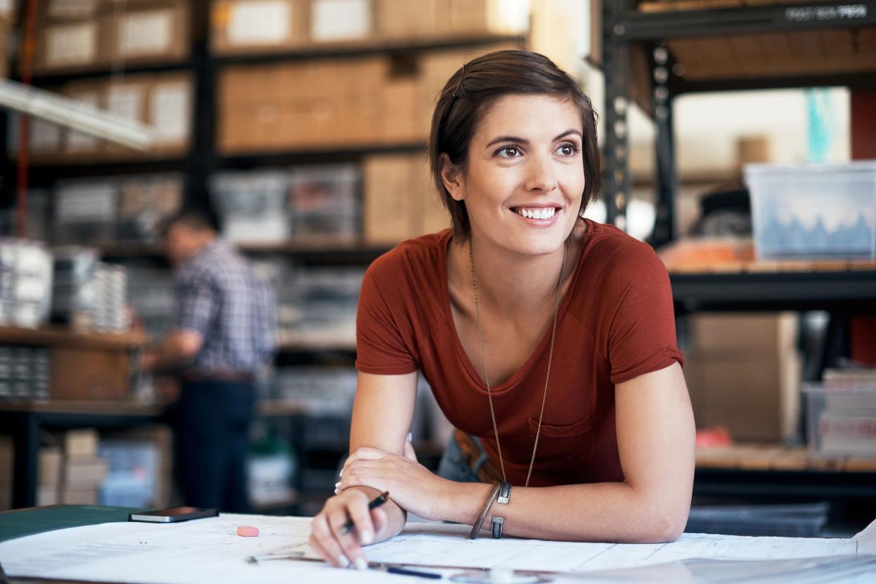 Satisfied young woman leaning over drafting table with work papers, with a blurred background of a warehouse