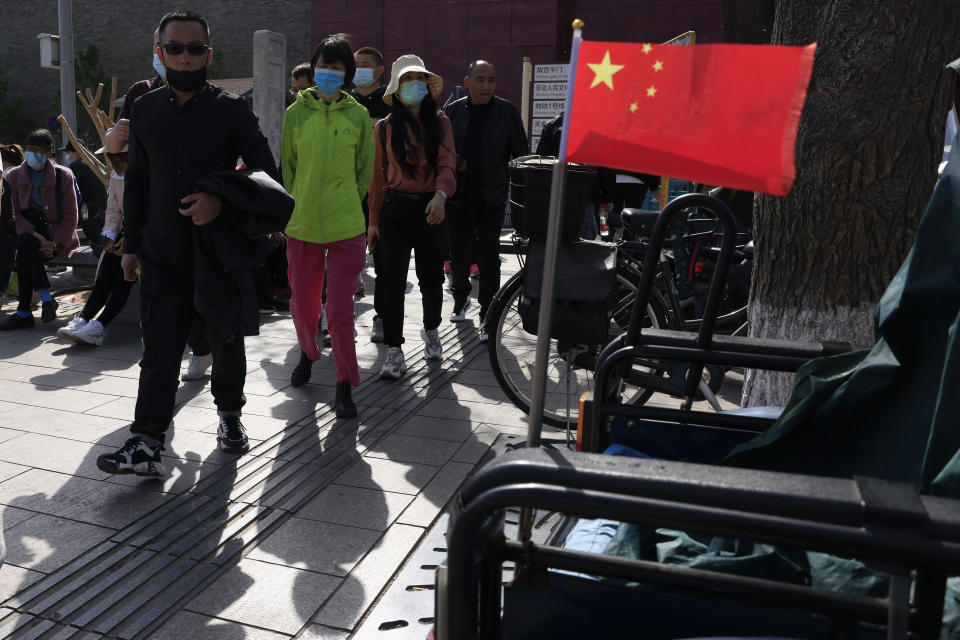 Residents in masks pass a Chinese national flag outside the Forbidden City where a bus is offering free coronavirus vaccinations in Beijing on Wednesday, April 14, 2021. China's success at controlling the outbreak has resulted in a population that has seemed almost reluctant to get vaccinated. It is now accelerating its inoculation campaign by offering incentives — free eggs, store coupons and discounts on groceries and merchandise — to those getting a shot. ​(AP Photo/Ng Han Guan)