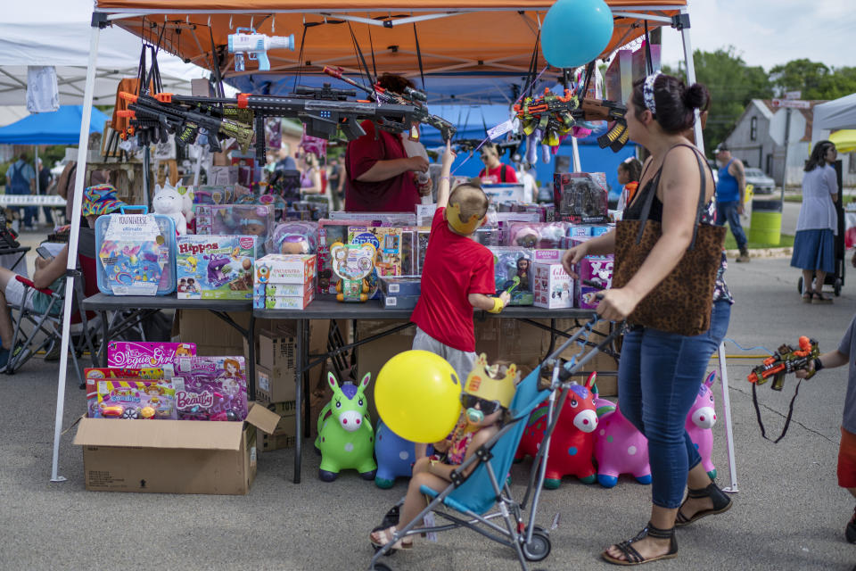 A boy reaches up for a toy machine gun for sale at a festival Saturday, June 10, 2023, in Jacksonville, Texas. At this festival, the Marine Corps booth down the street was auctioning off an AR-15 to raise money for a children's charity. A seller handed out free gun locks to anyone who buys his T-shirts, some supporting former President Donald Trump, others that declare: "God. Guns. Coffee." This is a place where people believe that guns are fundamental to their identity, that guns protect their families. (AP Photo/David Goldman)