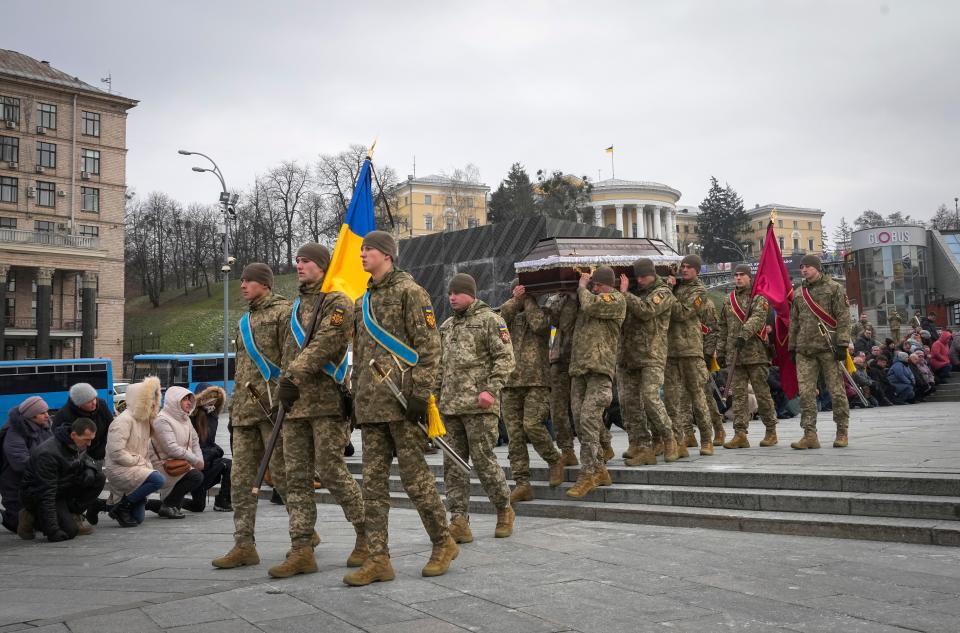 People kneel as the Ukrainian servicemen carry the coffin of their comrade Oleh Yurchenko, killed in a battlefield with Russian forces in the Donetsk region during a commemoration ceremony in Independence Square in Kyiv, Ukraine, Sunday, Jan. 8, 2023.