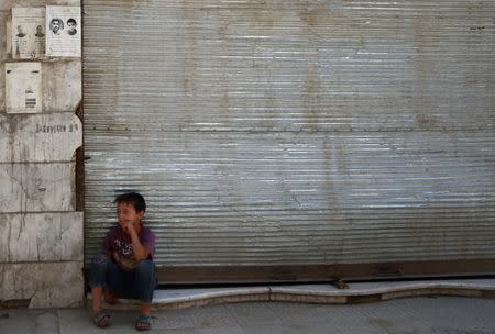 A Syrian child sits in front of a shop in the rebel held besieged Douma neighbourhood of Damascus, Syria July 23, 2017. REUTERS/Bassam Khabieh