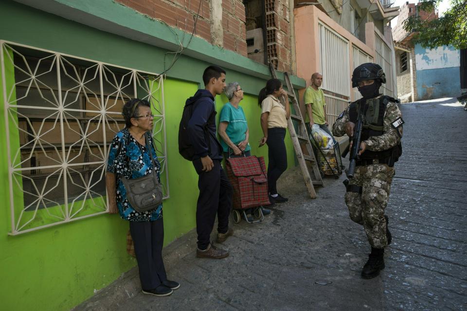 Residents stand near a wall as they watch a member of the National Police Action Force, or FAES, an elite commando unit created for anti-gang operations, patrol the Antimano neighborhood of Caracas, Venezuela, Tuesday, Jan. 29, 2019. Human Rights Watch has detailed widespread abuses by members of Venezuela's security forces in reports published in 2014 and 2017. (AP Photo/Rodrigo Abd)