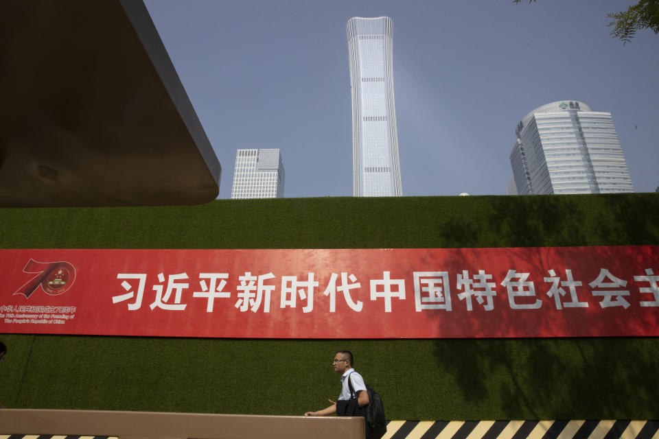 In this Friday, Sept. 27, 2019, photo, a man passes by a slogan for the upcoming 70th anniversary of the Founding of the People's Republic of China with the words "Xi Jinping New Era Socialism with Chinese Characteristics" in Beijing. Chinese President Xi Jinping has an ambitious goal for China: to achieve "national rejuvenation" as a strong and prosperous nation by 2049, which would be the 100th anniversary of Communist Party rule. One problem: U.S. President Donald Trump wants to make the United States great again too. (AP Photo/Ng Han Guan)