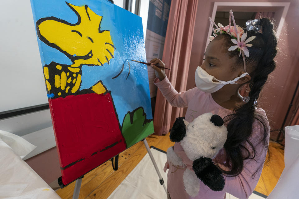 Kaley Williams, 8, paints a panel of a "Peanuts" mural that will be placed in the outpatient pediatric floor of One Brooklyn Health at Brookdale Hospital, Thursday, Oct. 1, 2020, in the Brooklyn borough of New York. The virus pandemic won't stop Charlie Brown, Snoopy or the "Peanuts" gang from marking an important birthday and they're hoping to raise the spirits of sick kids while they celebrate. The beloved comic marks its 70th anniversary this week with new lesson plans, a new TV show and a philanthropic push that includes donating "Peanuts" murals for kids to paint in 70 children's hospitals around the globe, from Brooklyn to Brazil. (AP Photo/Mary Altaffer)