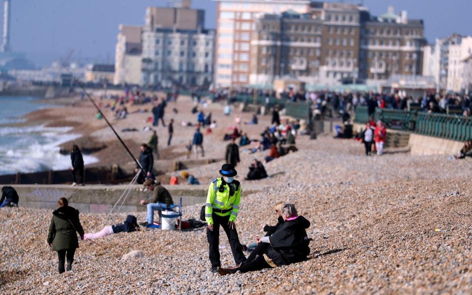 A community support officer speaks to people enjoying the sunshine on Brighton beach in Sussex in Sunday - PA/Steve Parsons 