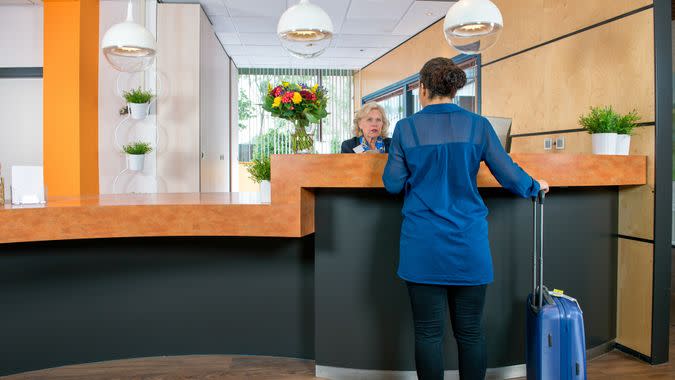 Young woman with a carry on bag at a check in desk, where a female attendant offers information and assistance.