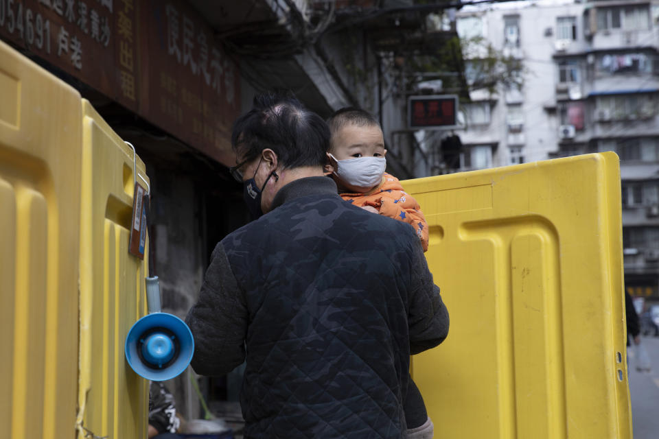 A child is carried between yellow barriers used to seal off a neighborhood in Wuhan in central China's Wuhan province on Wednesday, April 1, 2020. Skepticism about China’s reported coronavirus cases and deaths has swirled throughout the crisis, fueled by official efforts to quash bad news in the early days and a general distrust of the government. In any country, getting a complete picture of the infections amid the fog of war is virtually impossible. (AP Photo/Ng Han Guan)