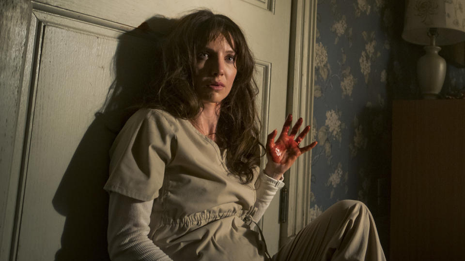 Annabelle Wallis sits with back against door holding a bloody hand up