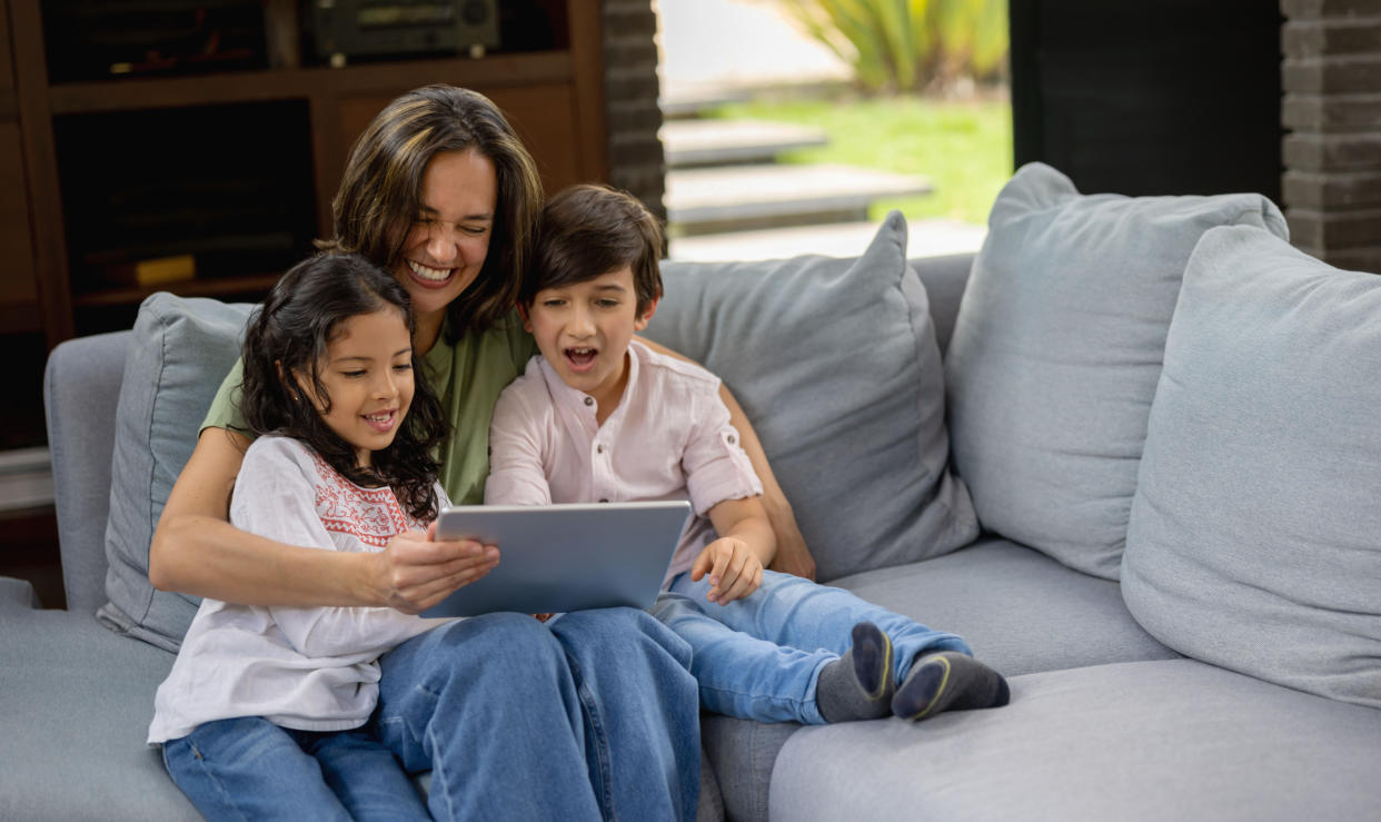 Happy Latin American mother at home watching videos online with her children on a tablet computer - lifestyle concepts