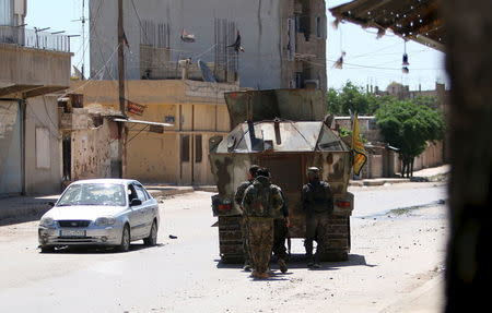 Kurdish fighters from the People's Protection Units (YPG) take cover behind a military vehicle as they advance in the southeast of Qamishli city, Syria, April 22, 2016. REUTERS/Rodi Said