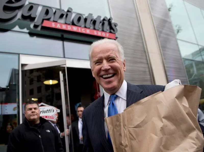 Joe Biden is all smiles, while holding a bag of food, outside of a Capriotti's sandwich shop in Washington, D.C.