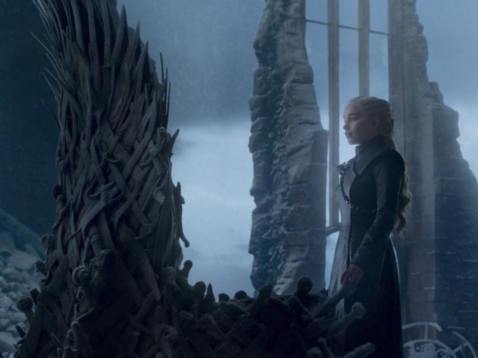Daenerys Targaryen (a young woman with blonde hair) standing in front of the large Iron Throne in the "Game of Thrones" series finale.