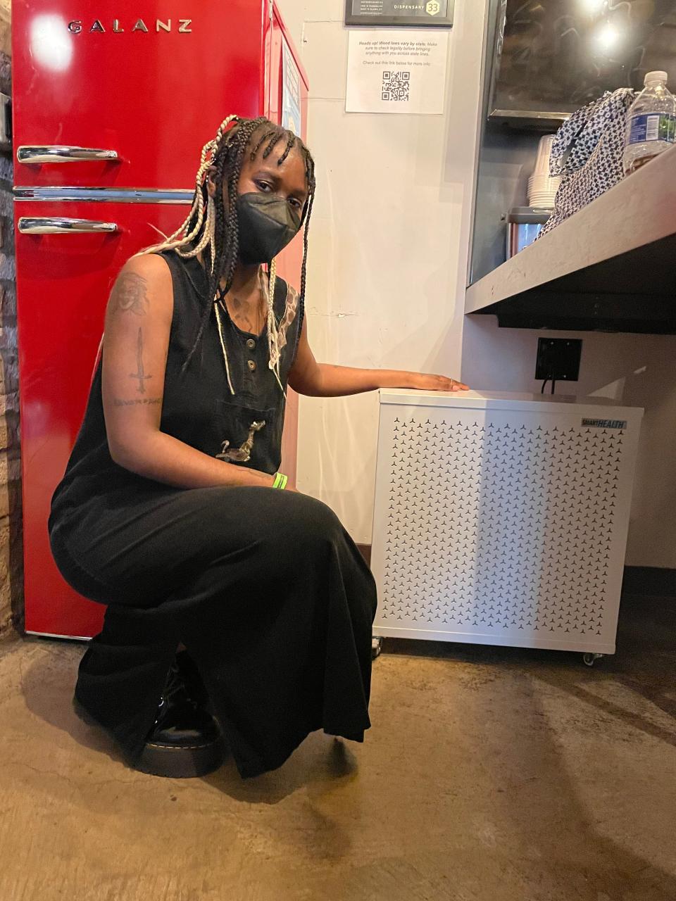 Kara Jackson, masked, with a Clean Air Club purifier in a green room.