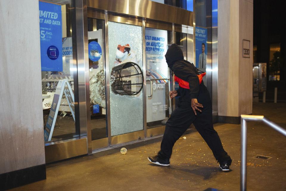 A young man throws a trash can through the window of an AT&T store Sunday, May 31, 2020, in New York. Demonstrators took to the streets of New York to protest the death of George Floyd, who died May 25 after he was pinned at the neck by a Minneapolis police officer. 5. (AP Photo/Kevin Hagen).