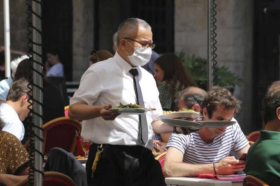 A restaurant employee serves meals in a restaurant of Saint Jean de Luz, southwestern France, Tuesday June 2, 2020. The French way of life resumes Tuesday with most virus-related restrictions easing as the country prepares for the summer holiday season amid the pandemic. Restaurants and cafes reopen Tuesday with a notable exception for the Paris region, the country's worst-affected by the virus, where many facilities will have to wait until June 22 to reopen. (AP Photo/Bob Edme)