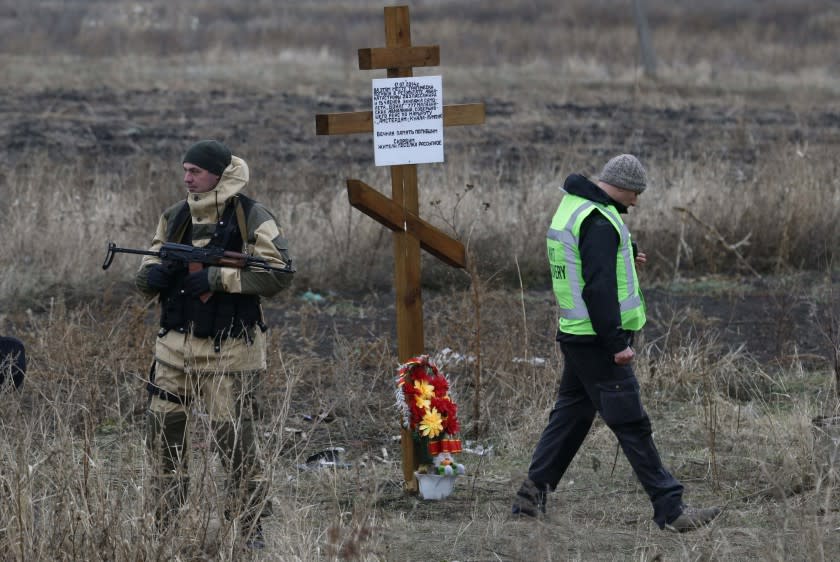 A member of the recovery team works at the site where the downed flight MH17 plane crashed near the village of Rozsypne as an armed security representing the self-proclaimed Donetsk People&#39;s Republic stands guard near a cross erected by local residents in