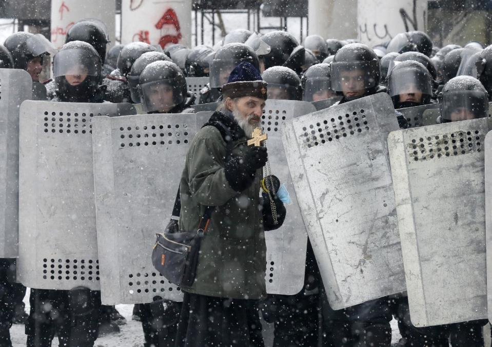 FILE In this file photo taken on Wednesday, Jan. 22, 2014, an Orthodox priest prays in front of police officers as they block a street after clashes in central Kiev, Ukraine. As a barricade of blazing tires belched thick black smoke, a line of priests stood between angry protesters and ominous riot police. Every freezing morning, priests sing prayers to demonstrators gathered on the Ukrainian capital's main square, a solemn and soothing interlude to vehement speeches calling for revolution.(AP Photo/Efrem Lukatsky, file)