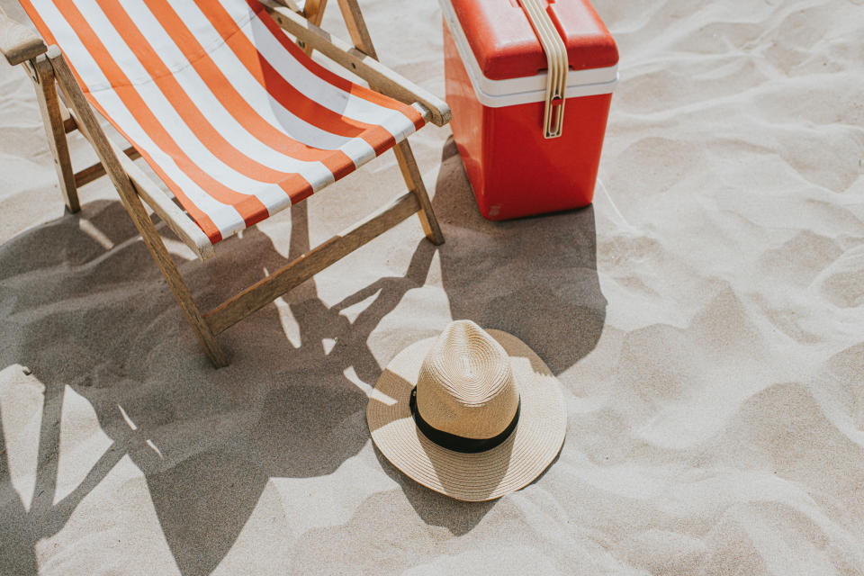 A striped beach chair, a hat, and a cooler on a sandy beach