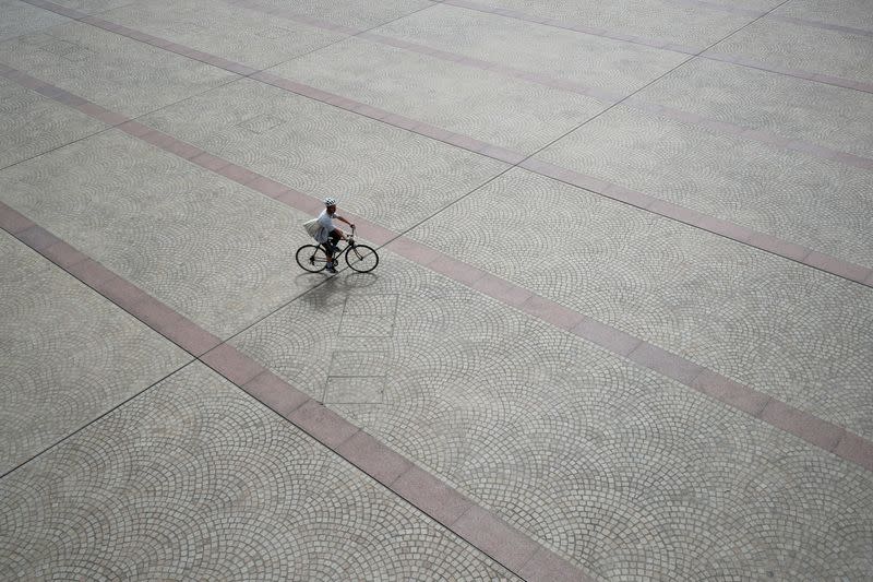 A person cycles across an open space in front of the steps of the Sydney Opera House