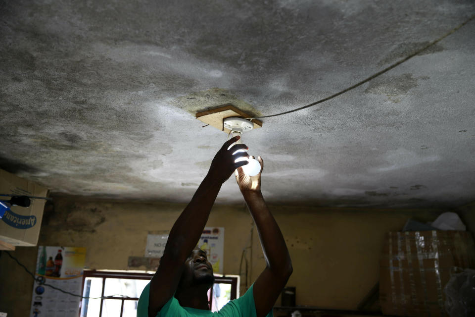 In this April 16, 2019 photo, Johny Legagneur charges a light bulb for a client at his shop in Petion-Ville, Haiti. Johny uses an inverter and generator to charge laptops, smartphones and rechargeable bulbs for a fee. Haiti's Bureau of Monetization of Development Aid Programs, started to buy oil on the global market, but it has now said that it has run out of operating funds and stopped regularly delivering fuel needed by power station operators to keep the lights on. ( AP Photo/Dieu Nalio Chery)