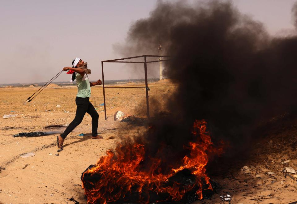 A Palestinian demonstrator hurls rocks next to burning tyres during a protest near to the border with IsraelAFP/Getty