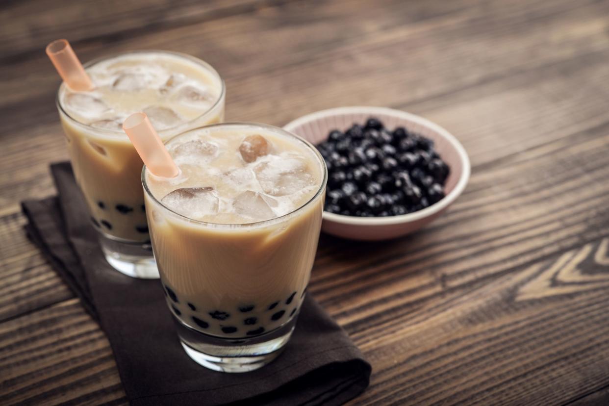 homemade boba milk tea, two glasses, with bowl of boba in background, on wooden surface