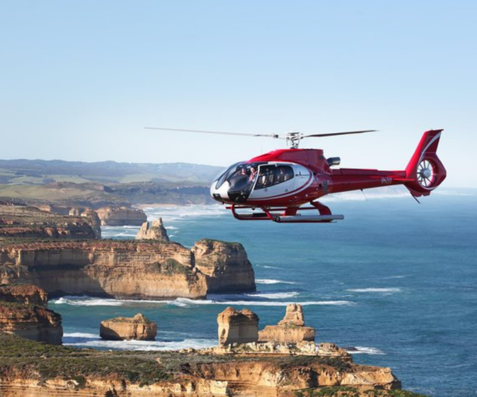 A red helicopter above the ocean over Victoria's great ocean road with a blue sky.