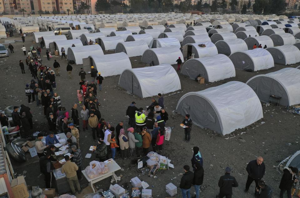 FILE - People who lost their houses in the devastating earthquake, lineup to receive food at a makeshift camp, in Iskenderun city, southern Turkey, on Feb. 14, 2023. Hundreds of thousands of people are seeking shelter after the Feb. 6 earthquake in southern Turkey left homes unlivable. Many survivors have been unable to find tents or containers dispatched to the region by the government and aid agencies, Instead they have sought refuge in any structure that can protect them from the winter conditions, including greenhouses, rail carriages and factories. (AP Photo/Hussein Malla)