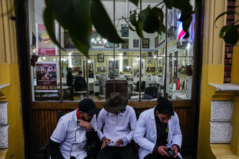 Barbers from the "Peluqueria Francesa" or French Hair Salon, sit outside their workplace in the Yungay neighborhood of Santiago, Chile, June 6, 2024. Yungay is a neighborhood with a mix of historic buildings, baroque facades and modern restaurants, and has also become a popular spot for the homeless. (AP Photo/Esteban Felix)