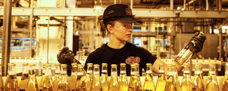 A beer factory worker inspecting bottles filled with beer.