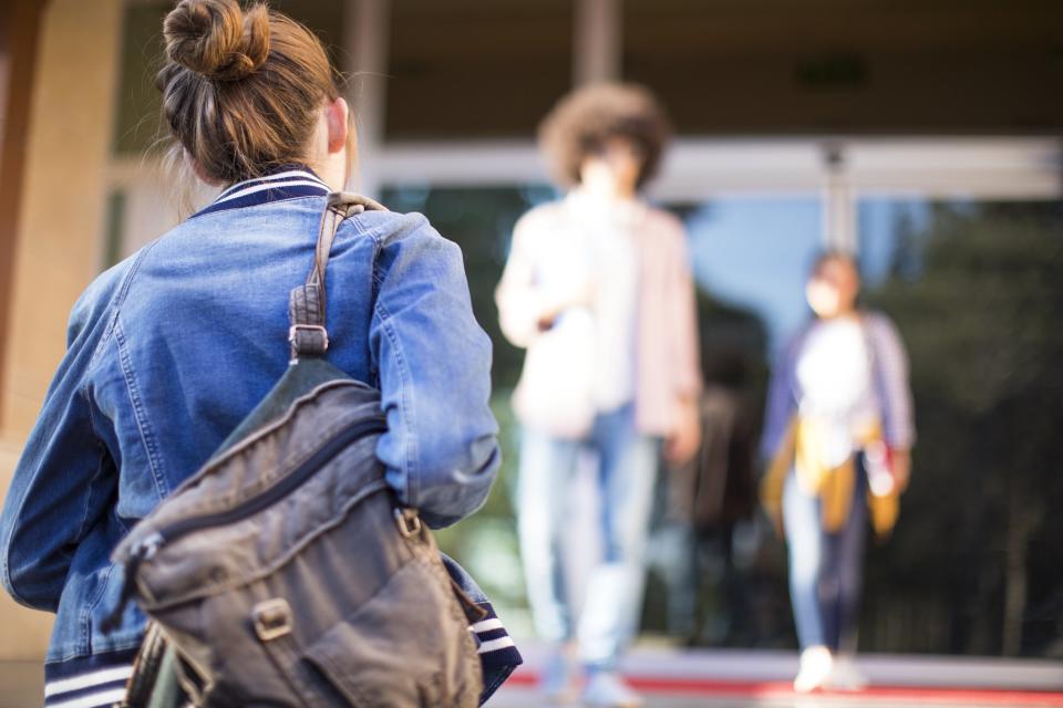 Female Student Walking Into School With Backpack Over Her Shoulder